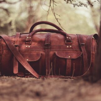 A leather weekender duffel set down on a woodland path
