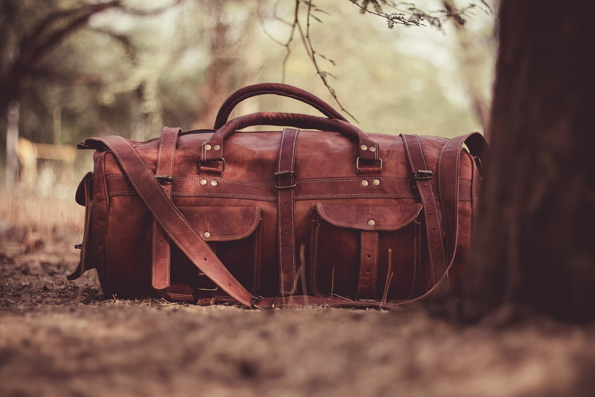A leather weekender duffel set down on a woodland path