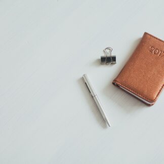 A tan leather pocket journal with a pen and a clip